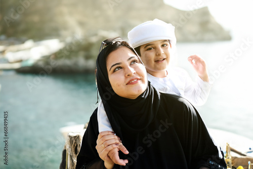 Arabic mother and son on a vacation trip during holidays on top of a island mountain with scenery background view of the ocean sea. Middle Eastern holiday trip concept