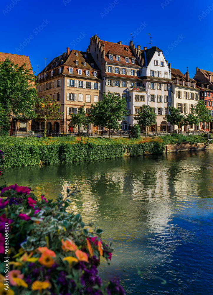 Fototapeta premium Ornate traditional half timbered houses with steep roofs above the Ill River with blooming flowers, the historic center of Strasbourg, Alsace, France