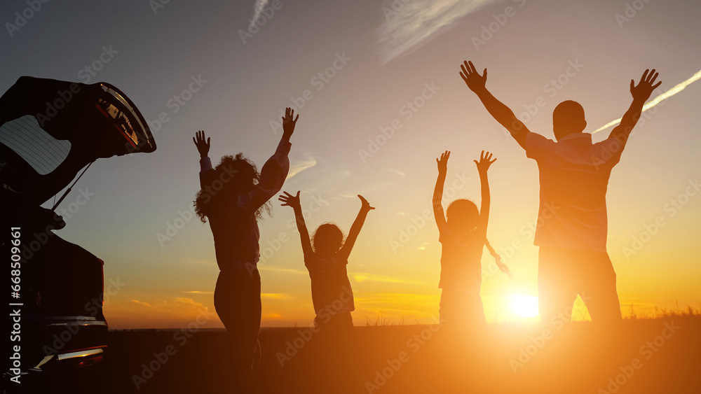 Happy parents with children raise hands standing near vehicle overlooking setting sun in evening. Concept of spending time with family and observing beauties of nature, sunlight