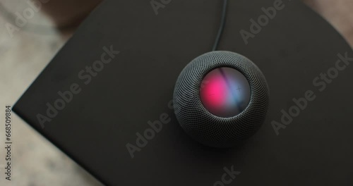 Using an HomePod Mini speaker - the smart speaker is reacting to voice listening to human commands and signalling its attention by the changing lights. Concept of a smart home. photo