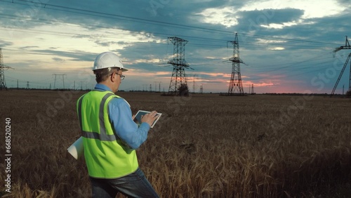 Manager in helmet types on tablet examining power transmission lines in field