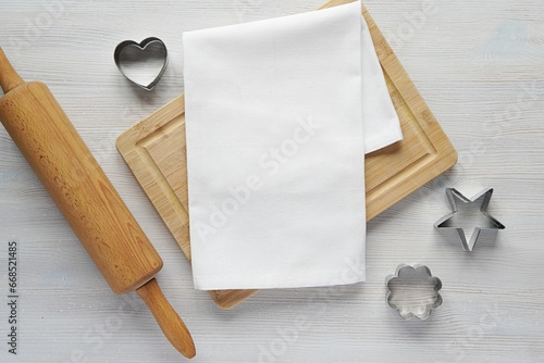 Obraz na płótnie White plain kitchen towel mockup for design or text presentation, wooden cutting board, kitchen utensils, natural flat lay composition on light color wooden table
