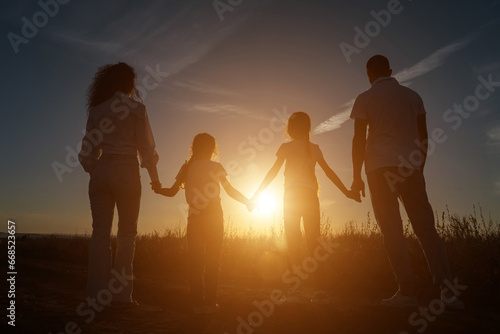 Happy family silhouettes holding hands in field with plants at sunset. Concept of active movement and spending time together in evening