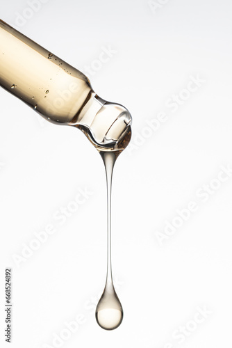 Pipette with serum, gel, oil or other cosmetic product with falling drop. Macro closeup