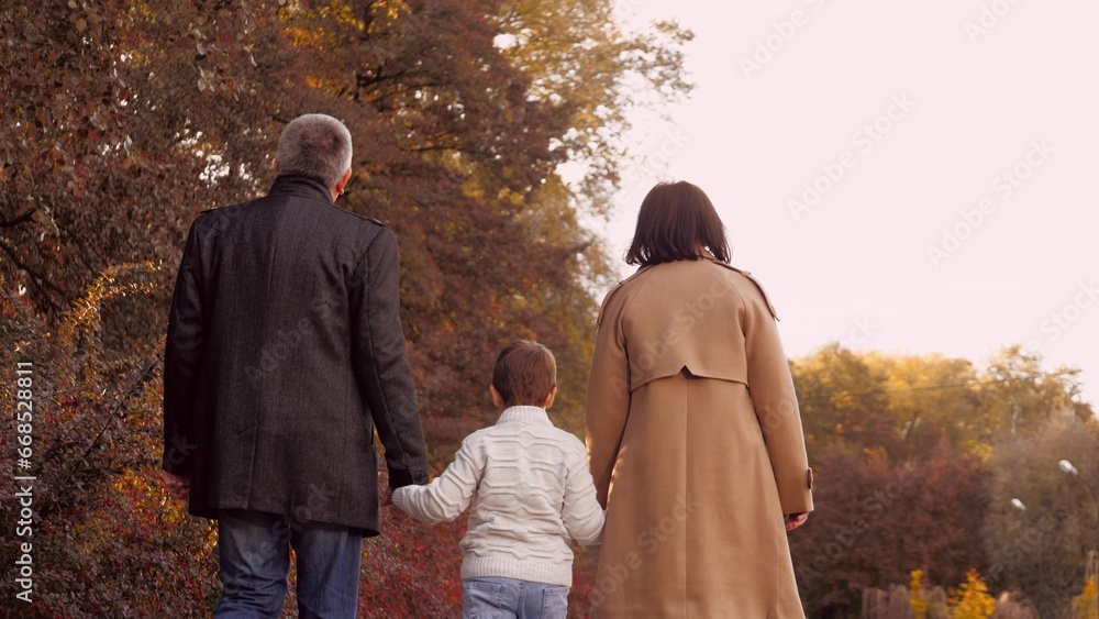 Family couple with little son in warm clothes walks in autumn park holding hands