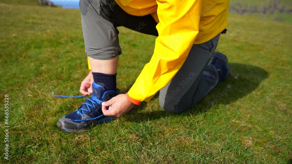 Close up shot of male hands tying a tall blue hiking boot on the grass Close up shot of male hands tying a tall blue hiking boot on the grass