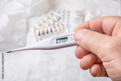 Hand holding a digital thermometer and pills on a white background. photo