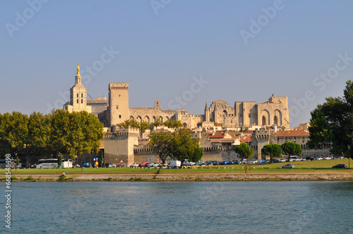 Papal Palace with several towers and the river Rhone embankment illuminated by the setting sun.