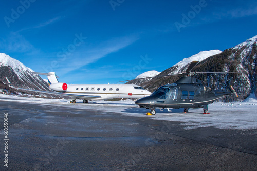 Luxury business jet and helicopter parked at the ramp in the engadin valley in the Swiss alps. The way to travel for the rich and wealthy. Especially in Winter to the ski resort in the mountains. .. photo