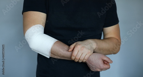 Male hand with tight elastic bandage on elbow closeup. Self help sprain concept photo