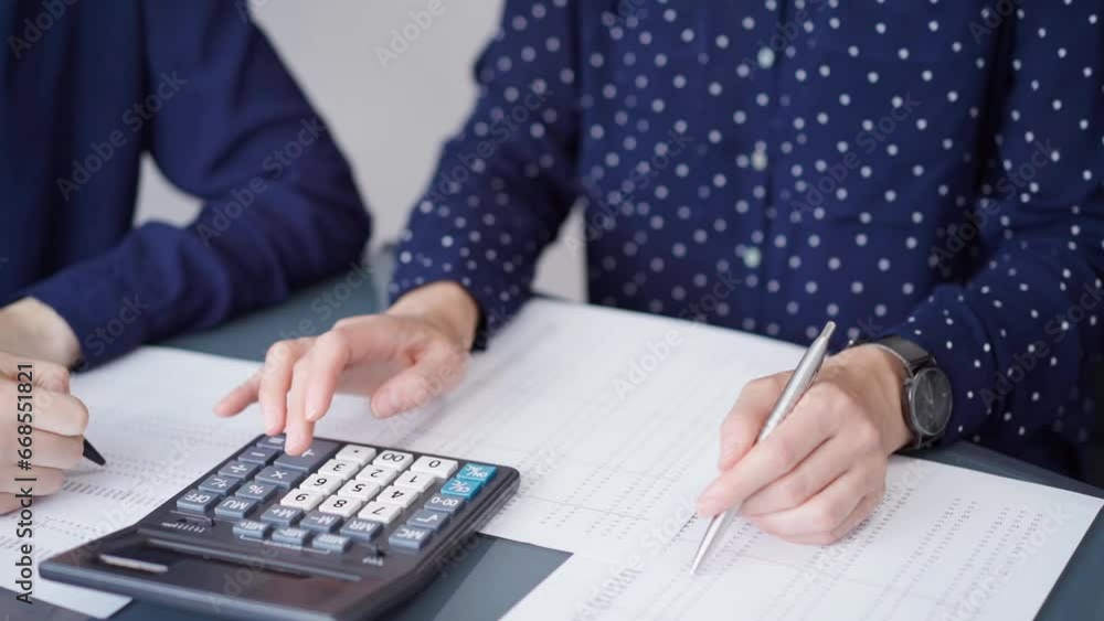 Two accountants dressed in blue are using calculator for counting taxes at grey desk in office, front side view. Teamwork in business audit and finance Two accountants dressed in blue are using calculator for counting taxes at grey desk in office, front side view. Teamwork in business audit and finance