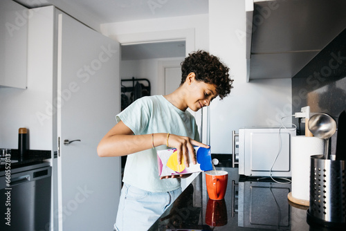 Ten years old girl pouring milk to a red mug in the kitchen. Girl at home preparing a cup of milk.