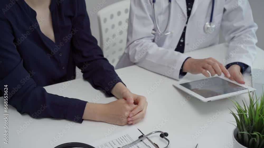 Doctor and patient sitting at the table and discussing something. The pediatrician in a blue dotted blouse and white medical coat using a tablet PC. Medicine concept Doctor and patient sitting at the table and discussing something. The pediatrician in a blue dotted blouse and white medical coat using a tablet PC. Medicine concept