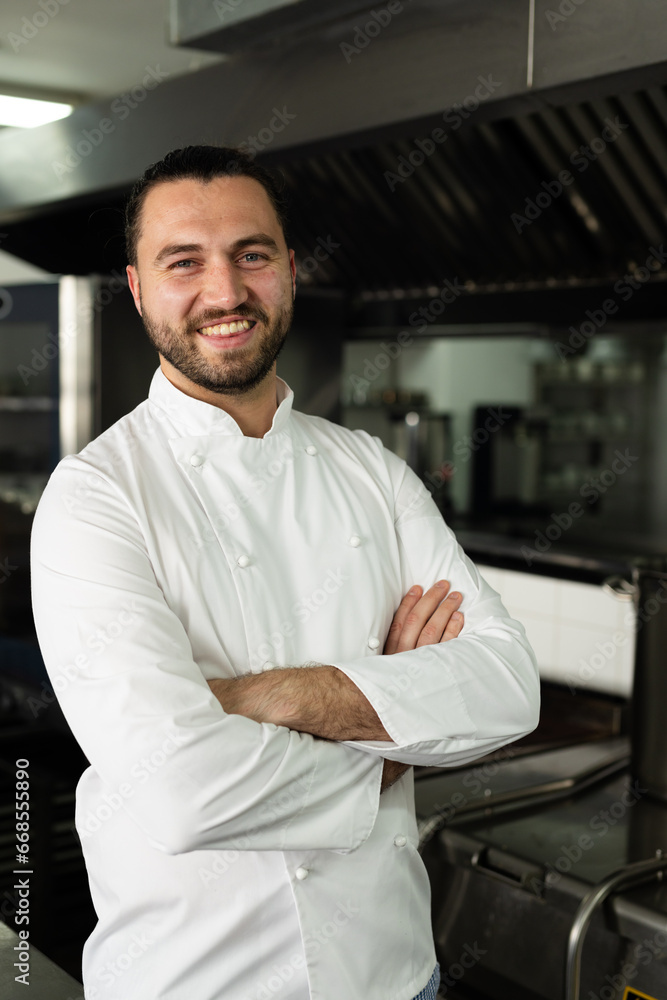 Portrait of happy caucasian male chef with arms crossed standing in kitchen at cooking school Portrait of happy caucasian male chef with arms crossed standing in kitchen at cooking school