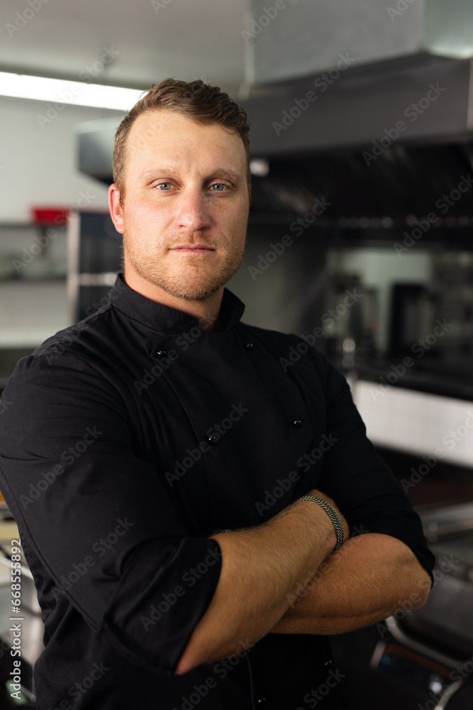 Confident caucasian male head chef in black uniform with arms crossed standing in kitchen Confident caucasian male head chef in black uniform with arms crossed standing in kitchen