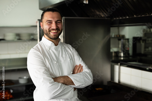 Portrait of smiling caucasian male chef with arms crossed standing in kitchen at cooking school photo