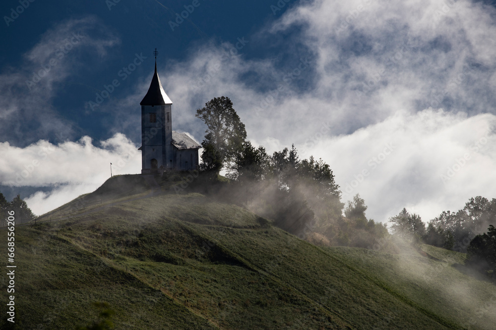 Jamnik, Slovenia - Magical foggy summer sunrise at Jamnik St.Primoz church. Jamnik, Slovenia - Magical foggy summer sunrise at Jamnik St.Primoz church.
