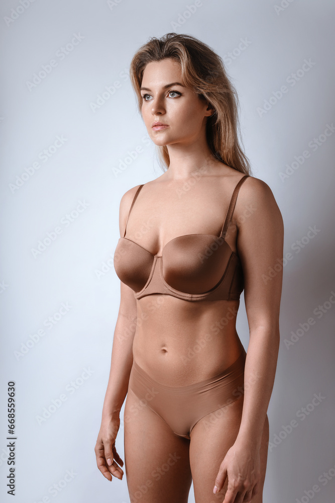 Fototapeta premium Portrait of young attractive woman wearing brown lingerie against gray background