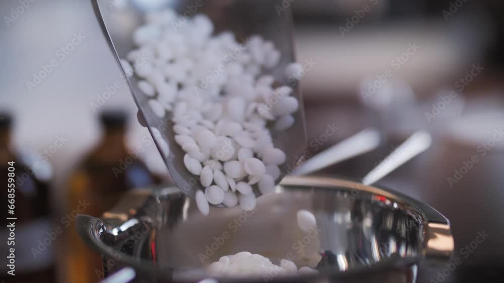 A metal measuring spoon pours soy wax into a metal pot, making candles