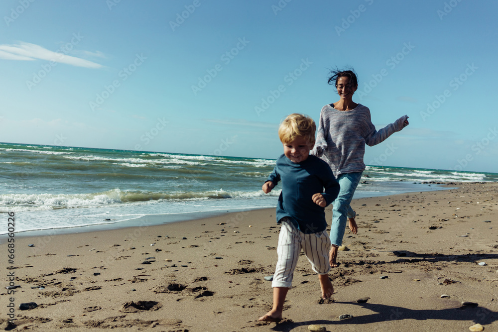 A young mother and her three-year-old son run, play, smile, and laugh on the seashore. A young mother and her three-year-old son run, play, smile, and laugh on the seashore.