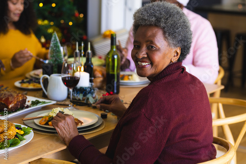 African american senior woman smiling at family christmas dinner in decorated dining room at home photo