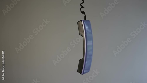 An abandoned landline telephone handset hangs on a cord on a gray background. The telephone receiver is hanging and dangling in the air. Unfinished phone conversation. photo