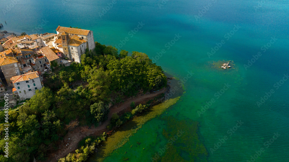 Aerial view of the collegiate church of Santa Maria Assunta in the historic center of Anguillara,in the metropolitan city of Rome, Italy. It's a Catholic church located on the shores of Lake Bracciano - obrazy, fototapety, plakaty 