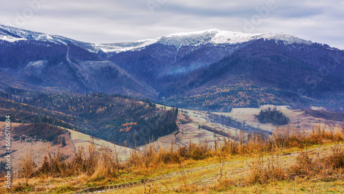 countryside landscape with snow capped tops in the distance. gloomy scenery of borzhava ridge with overcast sky in late autumn © Pellinni
