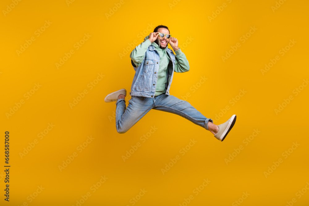 Full length photo of handsome cool guy hispanic run jumping touching his sunglass positive enjoy sale isolated on yellow color background