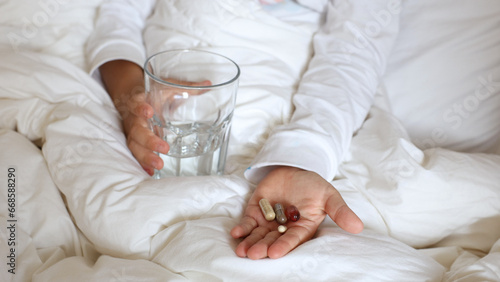 Closeup child hands palm hold glass water and medical pills. Sick Kid lying in bed ready taking medicine, vitamin mineral supplements,nutrition,health care, treatment.