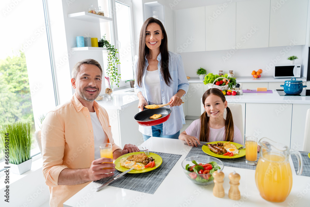 Photo of friendly family cute small daughter peaceful parents prepare eat yummy dish drink juice morning kitchen room inside Photo of friendly family cute small daughter peaceful parents prepare eat yummy dish drink juice morning kitchen room inside