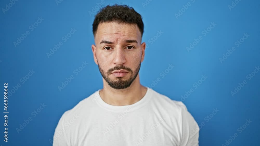 Young arab man standing with serious expression over isolated blue background Young arab man standing with serious expression over isolated blue background