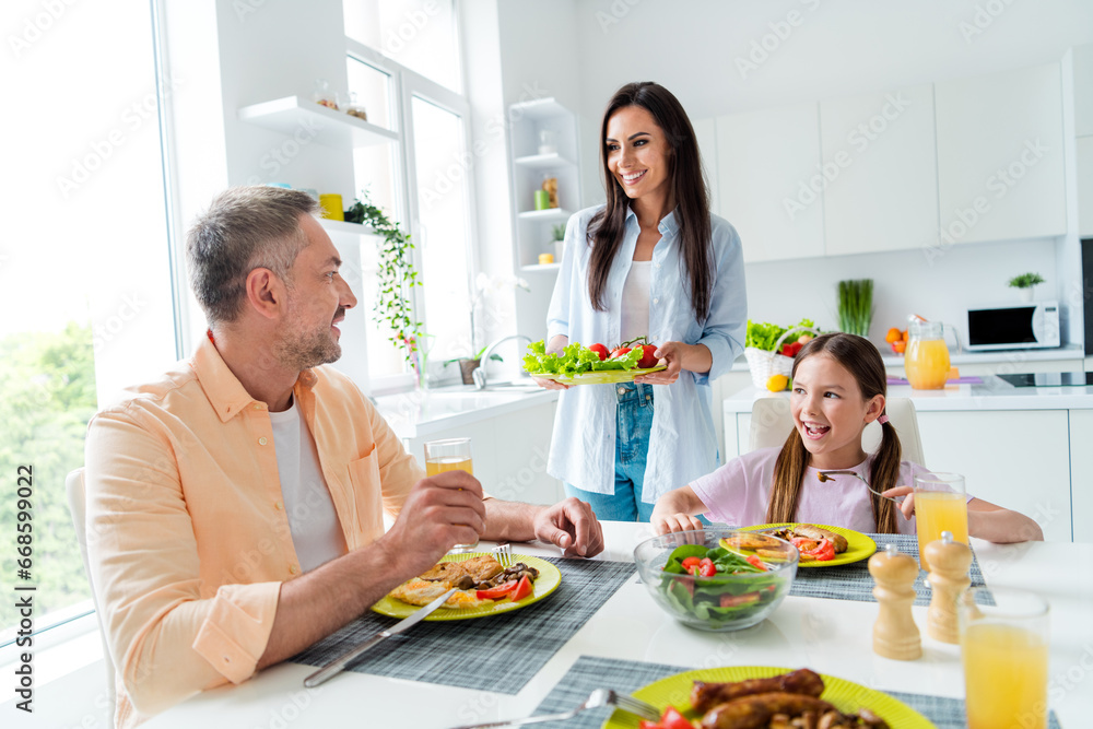 Photo of little girl peaceful parents dining room table eat domestic dish fresh vegetables enjoy cozy atmosphere indoors