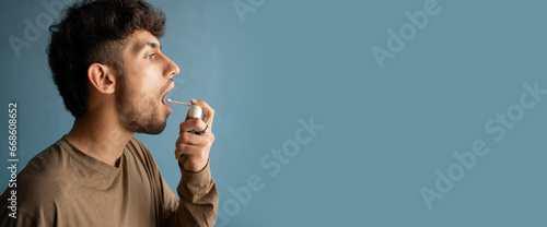 Arabic young man using throat spray isolated on blue background. Banner. photo
