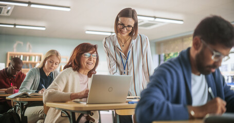 Helpful Young Teacher Talking with a Senior Woman, Helping to Find a Solution for a Test Course Assignment. Multiethnic Women and Men of Different Age Acquiring New Academic Skills in Classroom