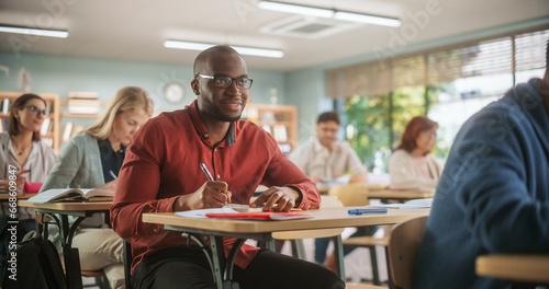 African Man Writing Down Notes in Notebook And Smiling. Group of International Mature Students Studying in Classroom. Adult Training Center Help People to Develop New Useful Skills Throughout Life photo