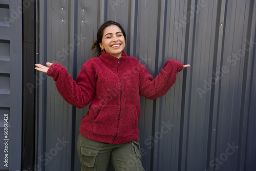 Young indian woman wearing red warm winter jacket. Standing with open arms isolated over black background