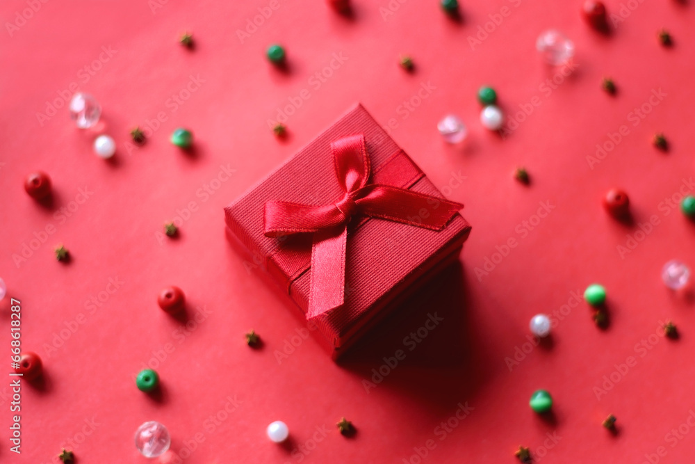Red present and various beads on red background. Selective focus. Red present and various beads on red background. Selective focus.