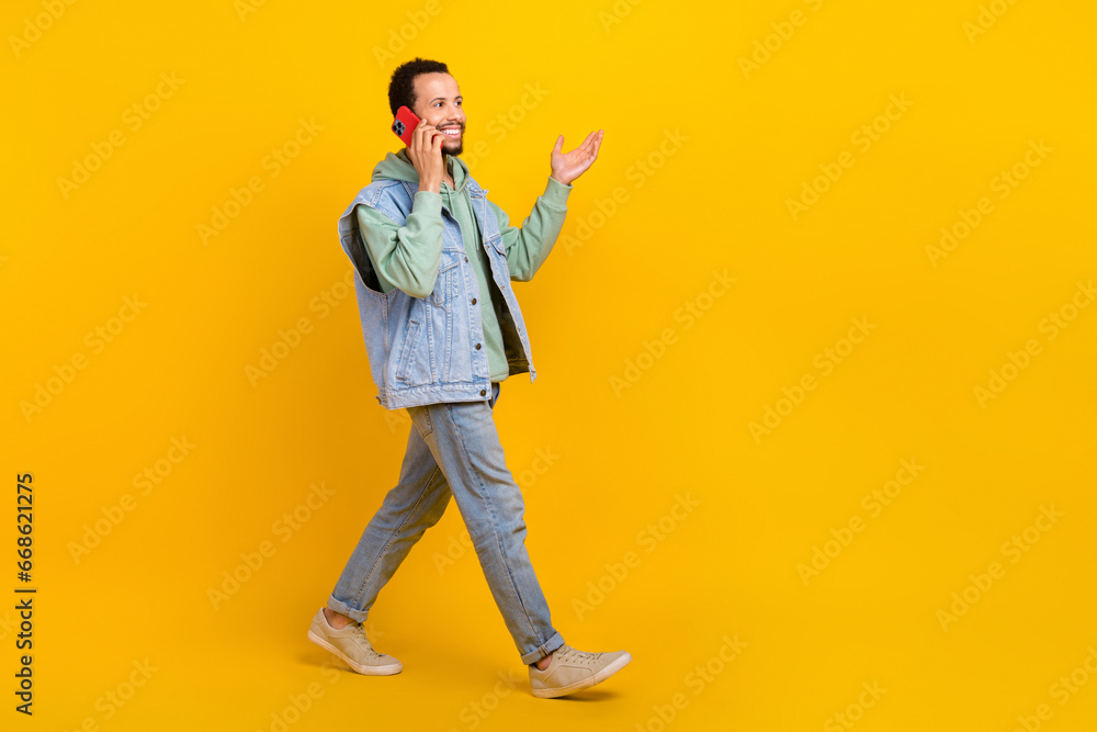Fototapeta premium Full length cadre of young hipster denim street style walking boyfriend calling friends gadget phone isolated on yellow color background