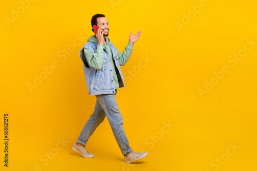 Full length cadre of young hipster denim street style walking boyfriend calling friends gadget phone isolated on yellow color background