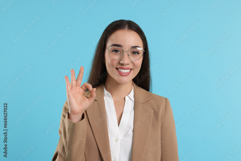 Beautiful woman in glasses showing OK gesture on turquoise background Beautiful woman in glasses showing OK gesture on turquoise background
