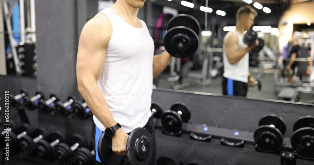 Man raises his arms with dumbbells in gym. Physical and muscle training for bodybuilding Man raises his arms with dumbbells in gym. Physical and muscle training for bodybuilding
