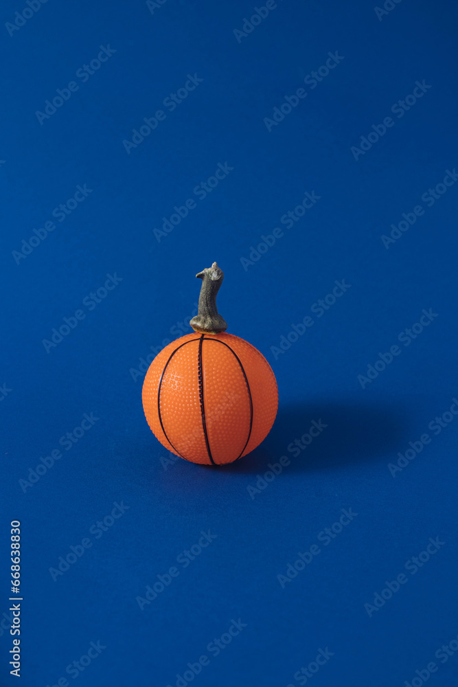 Orange basketball and pumpkin handle on a blue background. Minimal Halloween concept. Orange basketball and pumpkin handle on a blue background. Minimal Halloween concept.