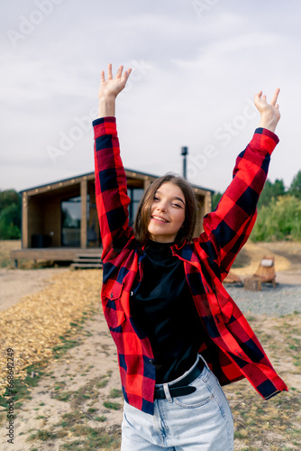 Portrait of a young happy girl dancing on the background of large wooden cottage in the forest steppe