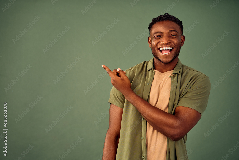 Choose this. African american male person with toothy smile on face pointing with index finger on empty space over green background. Handsome young guy indicating place for advertising text in studio. - obrazy, fototapety, plakaty 