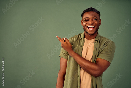 Choose this. African american male person with toothy smile on face pointing with index finger on empty space over green background. Handsome young guy indicating place for advertising text in studio. photo