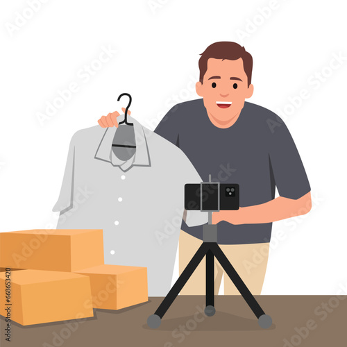 Young man is showing clothes in front of smartphone live streaming at his shop. Live online selling. Flat vector illustration isolated on white background