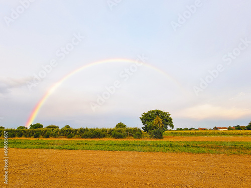 Tranquil agricultural landscape with a magical rainbow at sunset. Agrarian land of Croatia, Europe. Force of nature. Vibrant summertime photo wallpaper. Image of an exotic phenomenon. Beauty of earth.