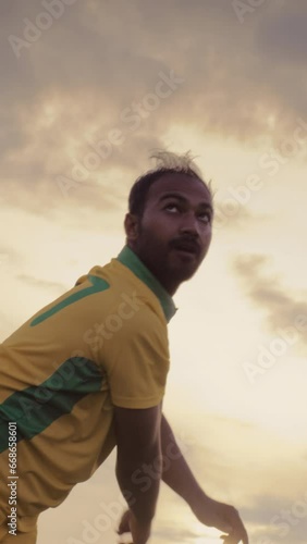 Vertical Screen: Portrait of a South Asian Cricket Player in Yellow and Green Uniform Throwing the Ball on a Pitch. Professional Indian Bowler is Focused, Aiming to Hit the Wicket With His Shot photo