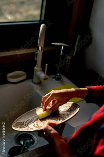 Close-up of a woman's hand with a foam sponge washing plates under the pressure of water in kitchen